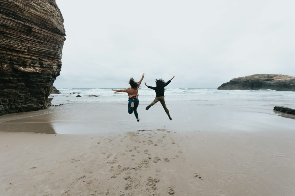 A couple of young women jumping in a wild beach with liberty during a sunny day with copy space